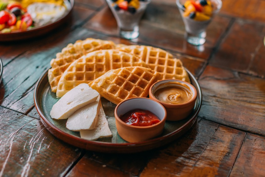 Prato com waffles dourados, queijo branco e potinhos de geleia e doce de leite